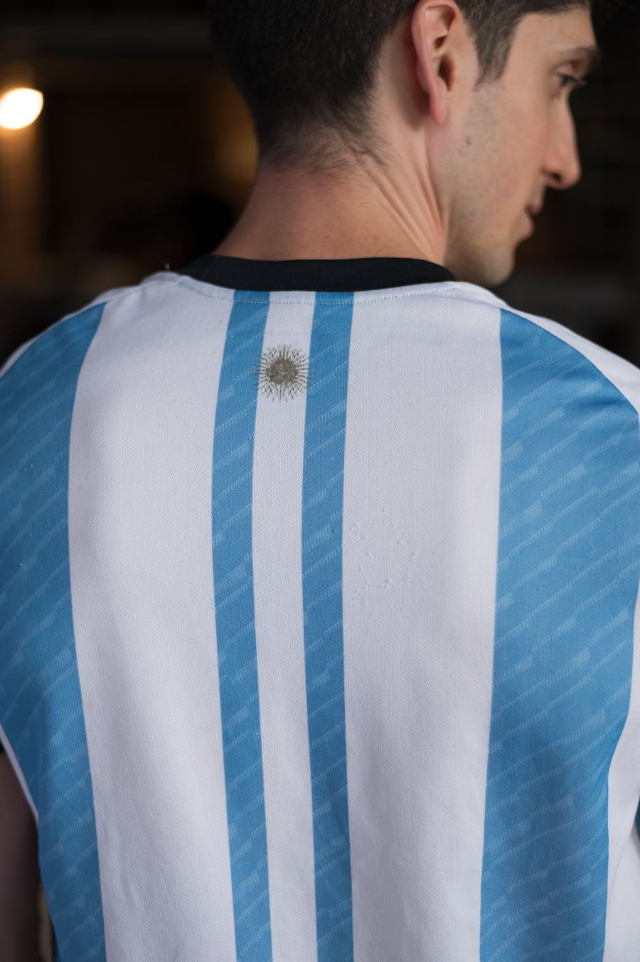 Vista de espalda de un aficionado con camiseta a rayas celestes personalizada con nombre y dorsal