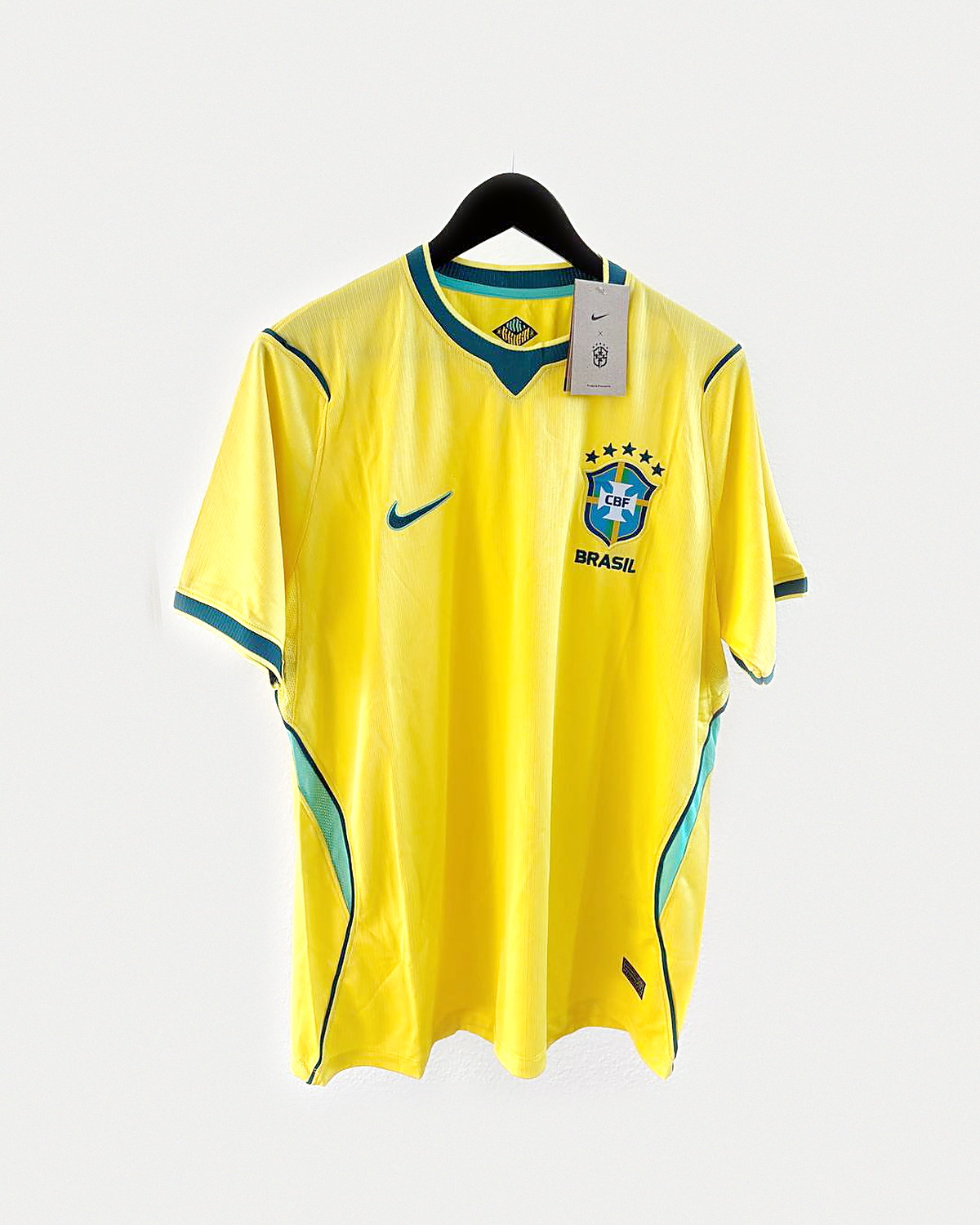 Camiseta de fútbol amarilla con ribetes verdes y escudo bordado en el pecho, colgada en una percha sobre pared clara
